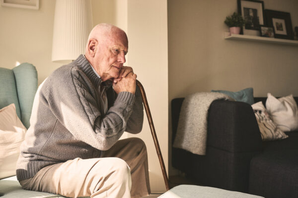 Thoughtful elderly man sitting alone at home with his walking cane