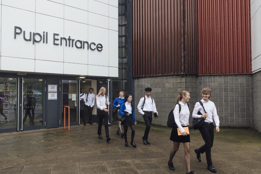 Students wearing school uniform, leaving school for the day in Gateshead, North East England. They are talking to each other while walking out of the building.