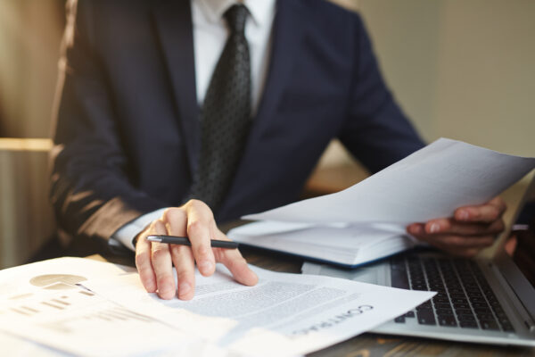 Closeup portrait of unrecognizable successful businessman wearing black formal suit reviewing finance statistics and contract documents at desk