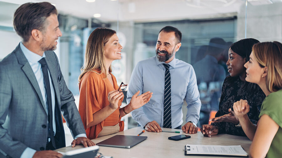 Five business people around a table, standing, smiling and discussing business