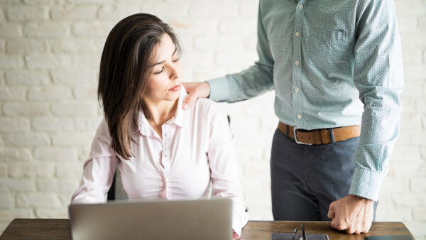 Woman at her desk and male colleague touching her shoulder