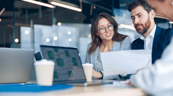 Female and male colleagues, in an office, looking at a laptop and documents