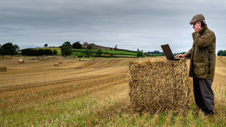 A farmer on a hay bale with a laptop