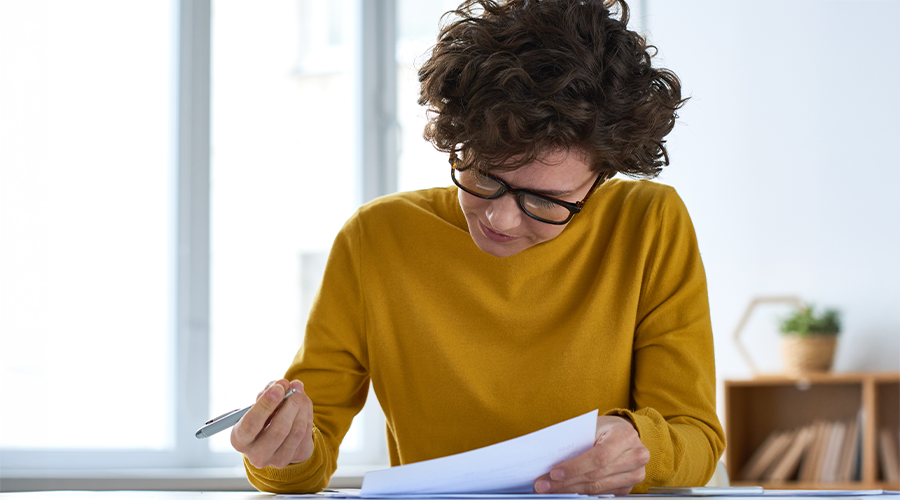 Female with yellow shirt on and glasses reading a document