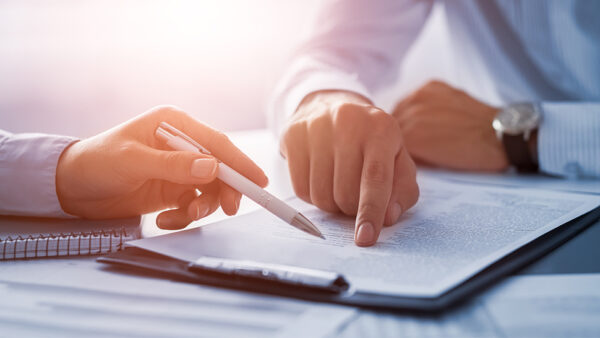 two people looking over a spreadsheet, pointing at writing on the spreadsheet