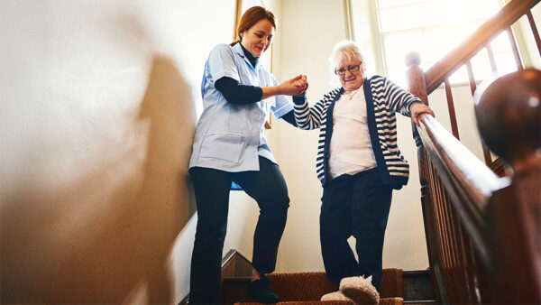 Social carer helping elderly person walking down the stairs