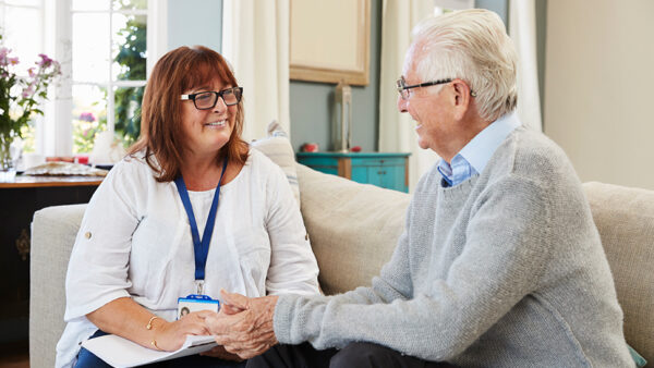 Social carer talking to elderly person on the sofa