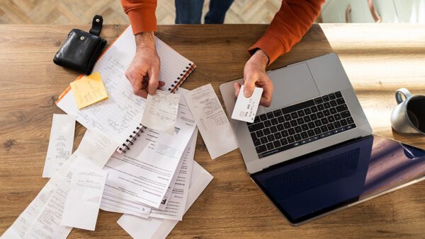 Person looking through notes and files on a desk, with their laptop opened